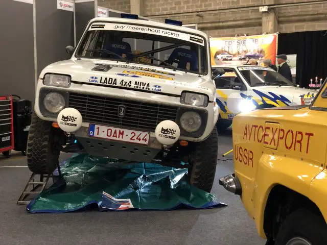 Een vintage Lada 4x4 Niva rallyauto te zien op het Antwerp Classic Salon 2020, met een gele rallyauto op de voorgrond.
