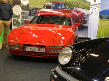 Rode Porsche 944 tentoongesteld op het Antwerp Classic Salon 2020 samen met andere klassieke auto's en aanwezigen.