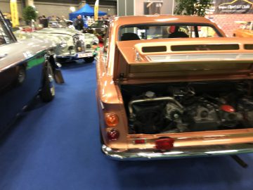 Klassieke auto's te zien op het Antwerp Classic Salon 2020, met de focus op een oranje auto met een open kofferbak waardoor de motor zichtbaar is.