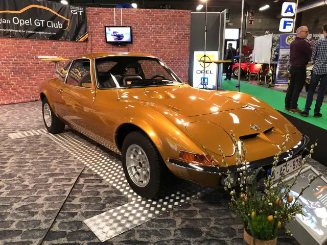 Vintage oranje sportwagen tentoongesteld op het Antwerp Classic Salon 2020 met toeschouwers op de achtergrond.