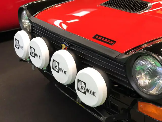 Close-up van een rode Abarth-auto met extra Cibie-rallylichten op het Antwerp Classic Salon 2020.