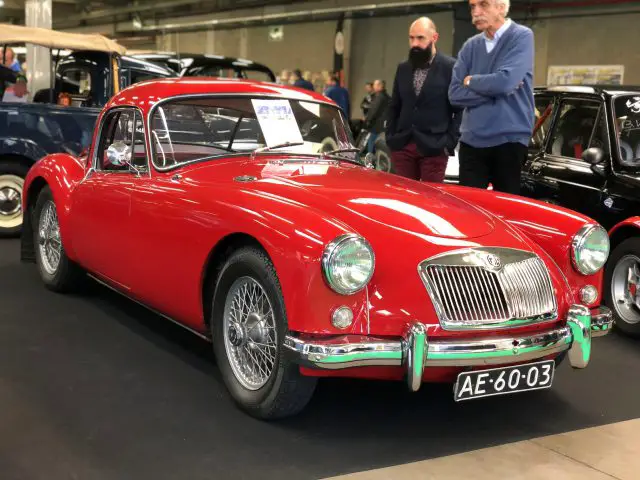 Een klassieke rode MG coupé te zien op het Antwerp Classic Salon 2020 met toeschouwers op de achtergrond.