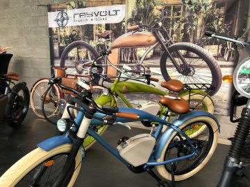 Een tentoonstelling van stijlvolle elektrische fietsen in verschillende kleuren in een fietsenwinkel met een bord met de tekst "Fischer Premium E-Bikes" op het Antwerp Classic Salon 2020.