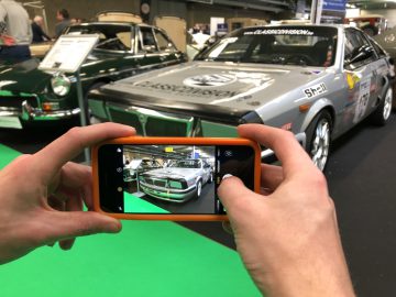 Een persoon die met een smartphone een foto maakt van klassieke racewagens tentoongesteld op het Antwerp Classic Salon 2020.