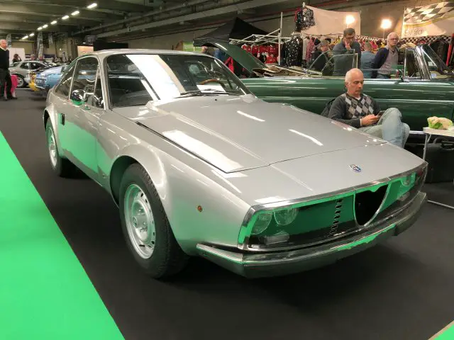 Een klassieke zilveren Alfa Romeo-auto te zien op het Antwerp Classic Salon 2020 met een toeschouwer op de achtergrond.