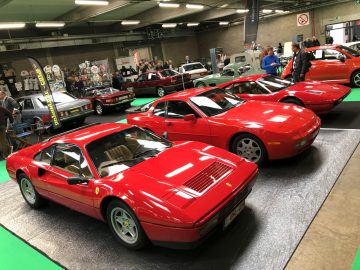 Een line-up van rode Ferrari-sportwagens te zien op het Antwerp Classic Salon 2020 met deelnemers op de achtergrond.
