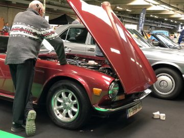 Man inspecteert de motor van een vintage rode auto op het Antwerp Classic Salon 2020.