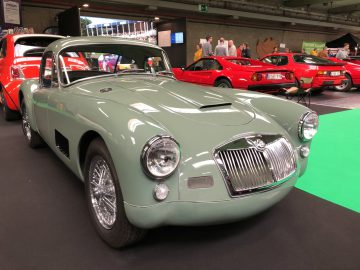 Vintage groene sportwagen tentoongesteld op het Antwerp Classic Salon 2020 met andere klassieke auto's op de achtergrond.