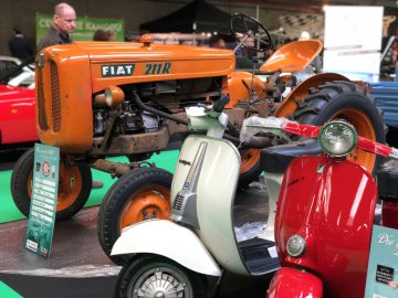Oranje vintage Fiat-tractor tentoongesteld naast klassieke scooters op de indoortentoonstelling Antwerp Classic Salon 2020.