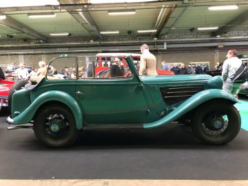 Groene vintage auto te zien op het Antwerp Classic Salon 2020, met mensen die op de achtergrond andere auto's bekijken.