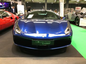 Een blauwe sportwagen te zien op het Antwerp Classic Salon 2020, met andere voertuigen en aanwezigen op de achtergrond.