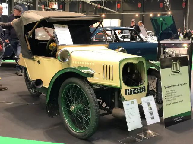 Vintage gele auto te zien op het Antwerp Classic Salon 2020 met toeschouwers op de achtergrond.