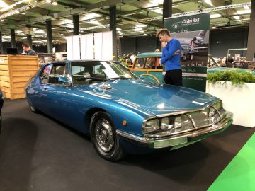 Een klassieke blauwe auto tentoongesteld op het Antwerp Classic Salon 2020 met aanwezigen in de buurt.