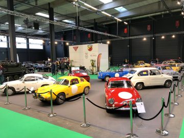 Klassieke auto’s te zien op het Antwerp Classic Salon 2020, met een levendig scala aan kleuren en stijlen, gescheiden door rongen op een groene vloerbedekking.