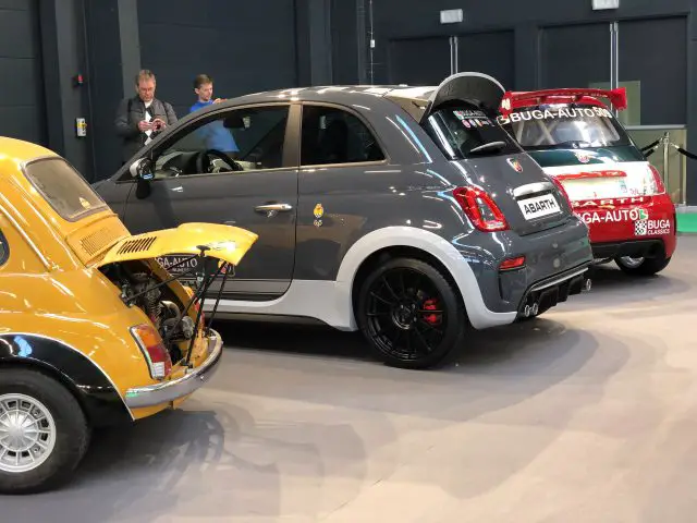 Een moderne Fiat Abarth-auto tentoongesteld naast een klassiek Fiat-model, met toeschouwers op de achtergrond op het Antwerp Classic Salon 2020.