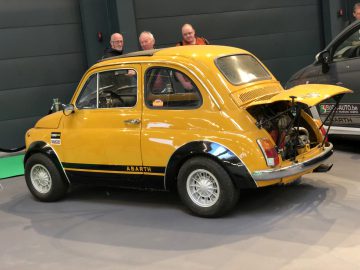 Een vintage Abarth Fiat 500 met de motor achterin tentoongesteld op het Antwerp Classic Salon 2020, geobserveerd door toeschouwers.