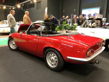 Rode vintage sportwagen tentoongesteld op het Antwerp Classic Salon 2020, met deelnemers op de achtergrond.