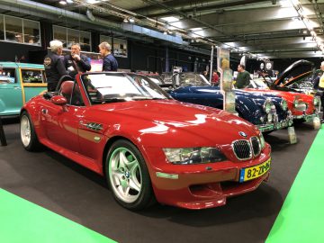 Rode BMW-cabriolet tentoongesteld op het Antwerp Classic Salon 2020 met deelnemers en verschillende klassieke auto's op de achtergrond.