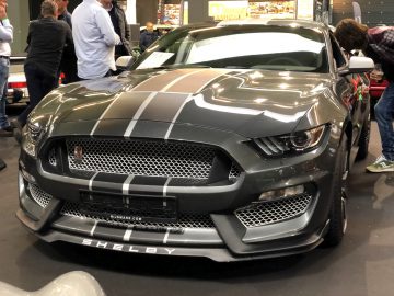 Een metaalgrijze Shelby Mustang tentoongesteld op de autoshow Antwerp Classic Salon 2020 met toeschouwers op de achtergrond.