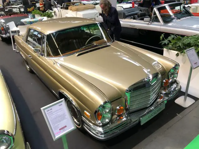 Vintage goudkleurige Mercedes-Benz tentoongesteld op het Antwerp Classic Salon 2020, terwijl een bezoeker hem onderzoekt.