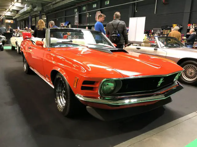 Oranje klassieke Mustang tentoongesteld op het Antwerp Classic Salon 2020 met toeschouwers op de achtergrond.
