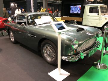 Een klassieke groene Aston Martin tentoongesteld op het Antwerp Classic Salon 2020 met een informatiestand ernaast.