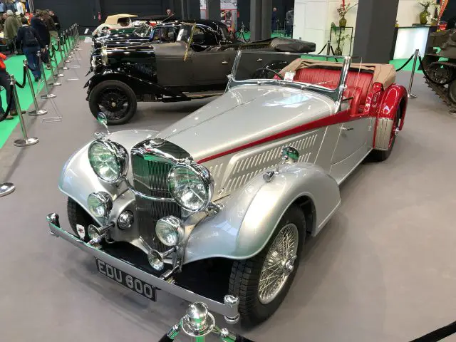 Klassieke zilveren en rode vintage auto te zien op het Antwerp Classic Salon 2020 met andere vintage voertuigen op de achtergrond.