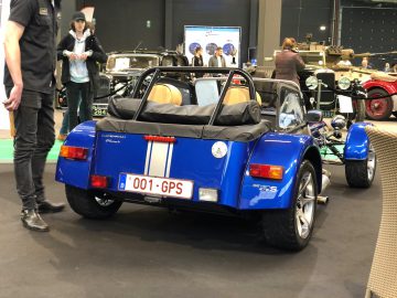 Blauwe vintage cabriolet tentoongesteld op het Antwerp Classic Salon 2020, terwijl bezoekers op de achtergrond andere klassieke voertuigen observeren.