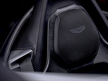 Close-up van de luxe stoel van een Aston Martin V12 Speedster met koolstofvezeldetails en een geborduurd embleem.