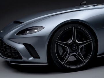 Close-up van de voorkant van een Aston Martin V12 Speedster, met de nadruk op het strakke ontwerp en de lichtmetalen velgen.