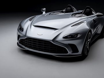 Een zilveren Aston Martin V12 Speedster converteerbare sportwagen tegen een grijze achtergrond.