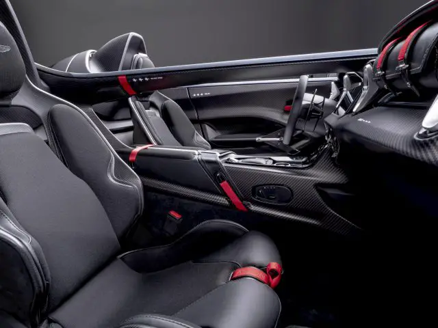 Luxe Aston Martin V12 Speedster-interieur met zwartleren stoelen met rode accenten en koolstofvezelbekleding.