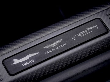 Een close-up van de interieurdetails van een Aston Martin V12 Speedster-auto, met merklogo's en modelaanduiding.