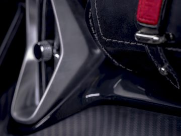 Een close-up van de veiligheidsgordel en koolstofvezeldetails van een Aston Martin V12 Speedster met het opschrift 'fia18', wat aangeeft dat wordt voldaan aan de FIA-normen van 2018.