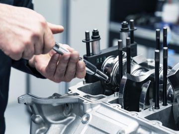 Een technicus assembleert of inspecteert een Aston Martin Valhalla-motor, waarbij hij zich met een stuk gereedschap in de hand op de interne componenten concentreert.