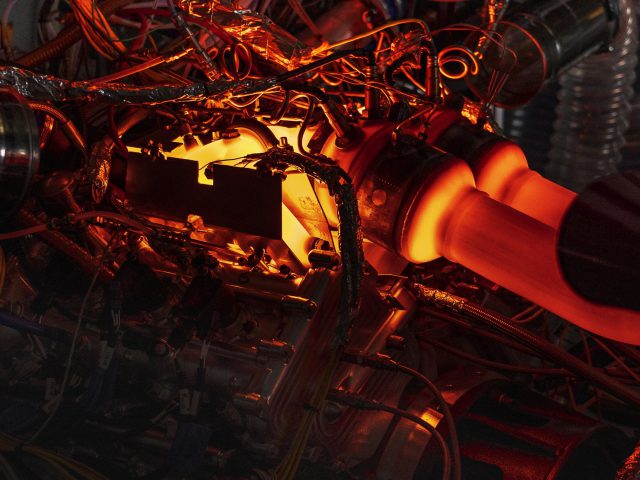 Complexe machines met gloeiende oranje elementen en een ingewikkeld netwerk van draden en buizen, die doen denken aan het verfijnde ontwerp van de Aston Martin Valhalla.
