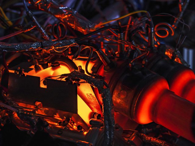 De complexe machinerie van Aston Martin Valhalla verlicht door rood licht, met ingewikkelde bedrading en mechanische componenten.