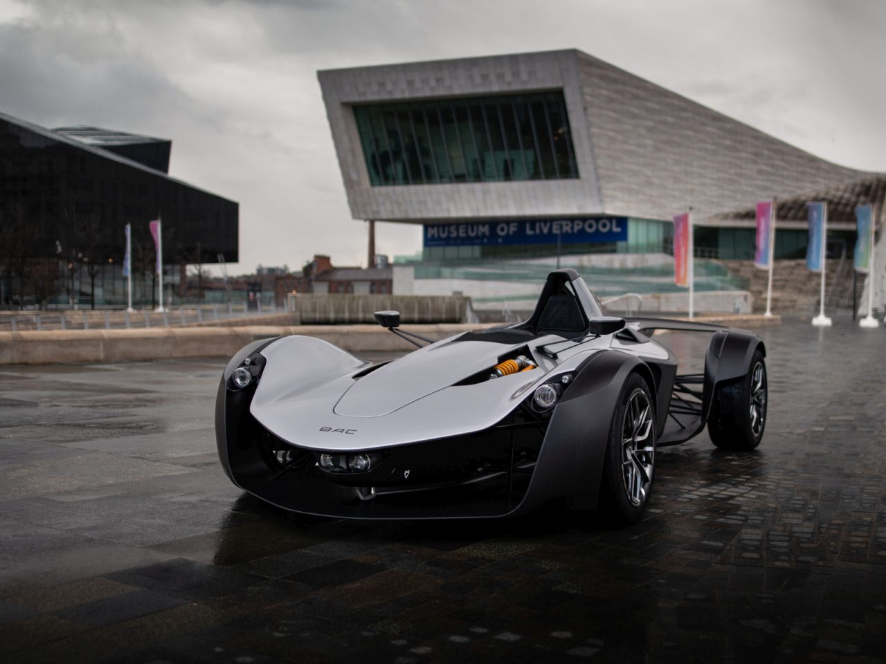 Een strakke zwarte BAC Mono-sportwagen geparkeerd voor het Museum van Liverpool op een bewolkte dag.