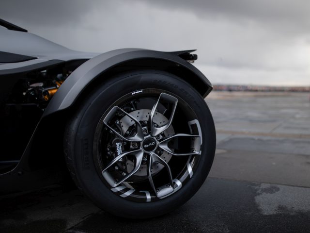 Close-up van het hoogwaardige voertuigwiel van een BAC Mono met opvallend lichtmetalen ontwerp, geparkeerd op een nat asfalt.