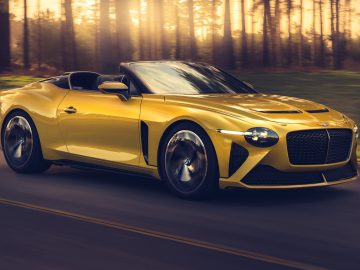 Een gele Bentley Mulliner Bacalar converteerbare sportwagen die bij zonsondergang op een weg rijdt.