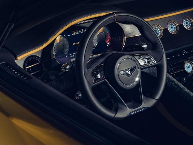 Luxe auto-interieur met een leren stuur met Bentley Mulliner Bacalar-logo, digitale displays en elegante houten lambrisering.