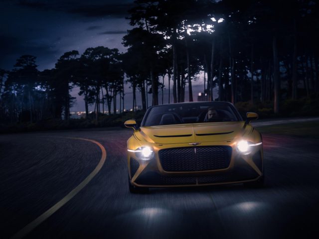 Een Bentley Mulliner Bacalar-sportwagen die 's nachts over een bochtige weg rijdt, verlicht door koplampen en een maanverlichte hemel.