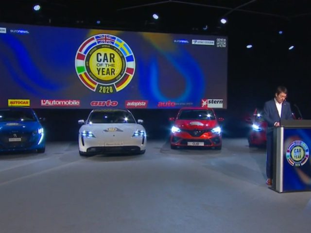 Presentator op een podium tijdens een 'Auto van het Jaar 2020' awardevenement met drie auto's op het podium.