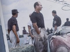 Mannen verzamelden zich rond raceauto's tijdens een buitenevenement met een Fangio-documentaire op Netflix.