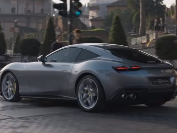 Een grijze Ferrari Roma rijdt door een stadsstraat met voetgangers op de achtergrond.