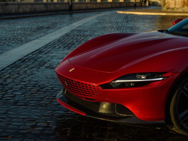 Rode Ferrari Roma geparkeerd op geplaveide straat bij zonsondergang.