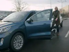 Vrouw verlaat een blauwe Ford-auto op een parkeerplaats.