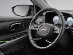 Modern Hyundai i20-interieur met een Hyundai-stuur met gemonteerde bedieningselementen, digitaal dashboard en zwarte bekleding met groene stiksels.