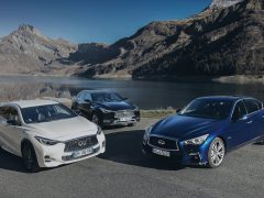 Drie Infiniti-auto's geparkeerd bij een bergmeer met een helderblauwe lucht op de achtergrond.