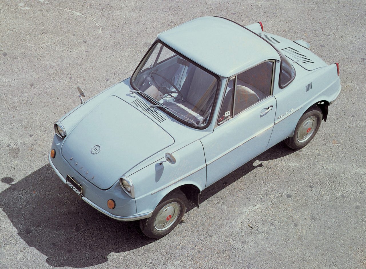 Vintage Mazda R360 compacte auto met een opvallende belvorm, geparkeerd op een betonnen ondergrond.